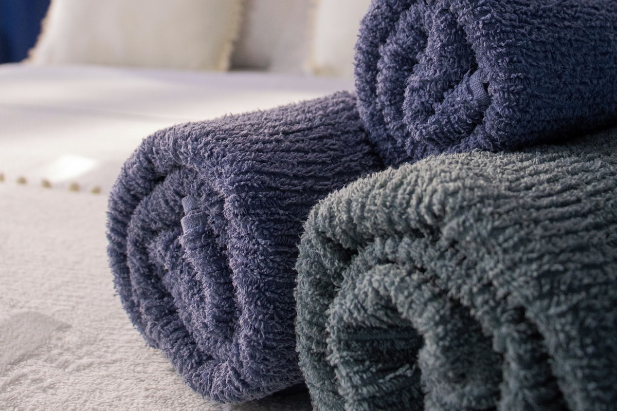 Una cama bien hecha con almohadas blancas y una toalla doblada en tonos azul y verde.