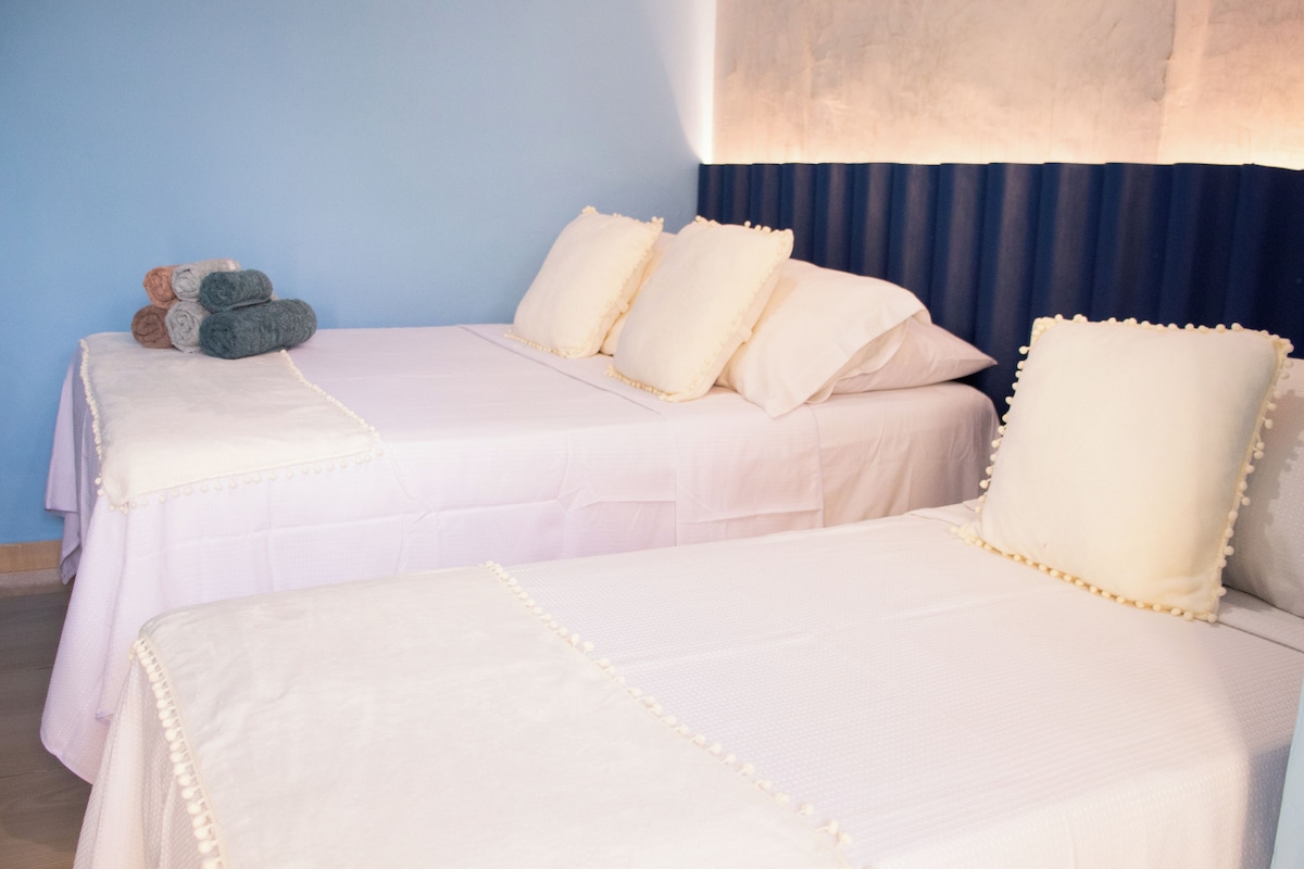 Habitación de hotel con dos camas, cada una con ropa blanca y almohadas decorativas.