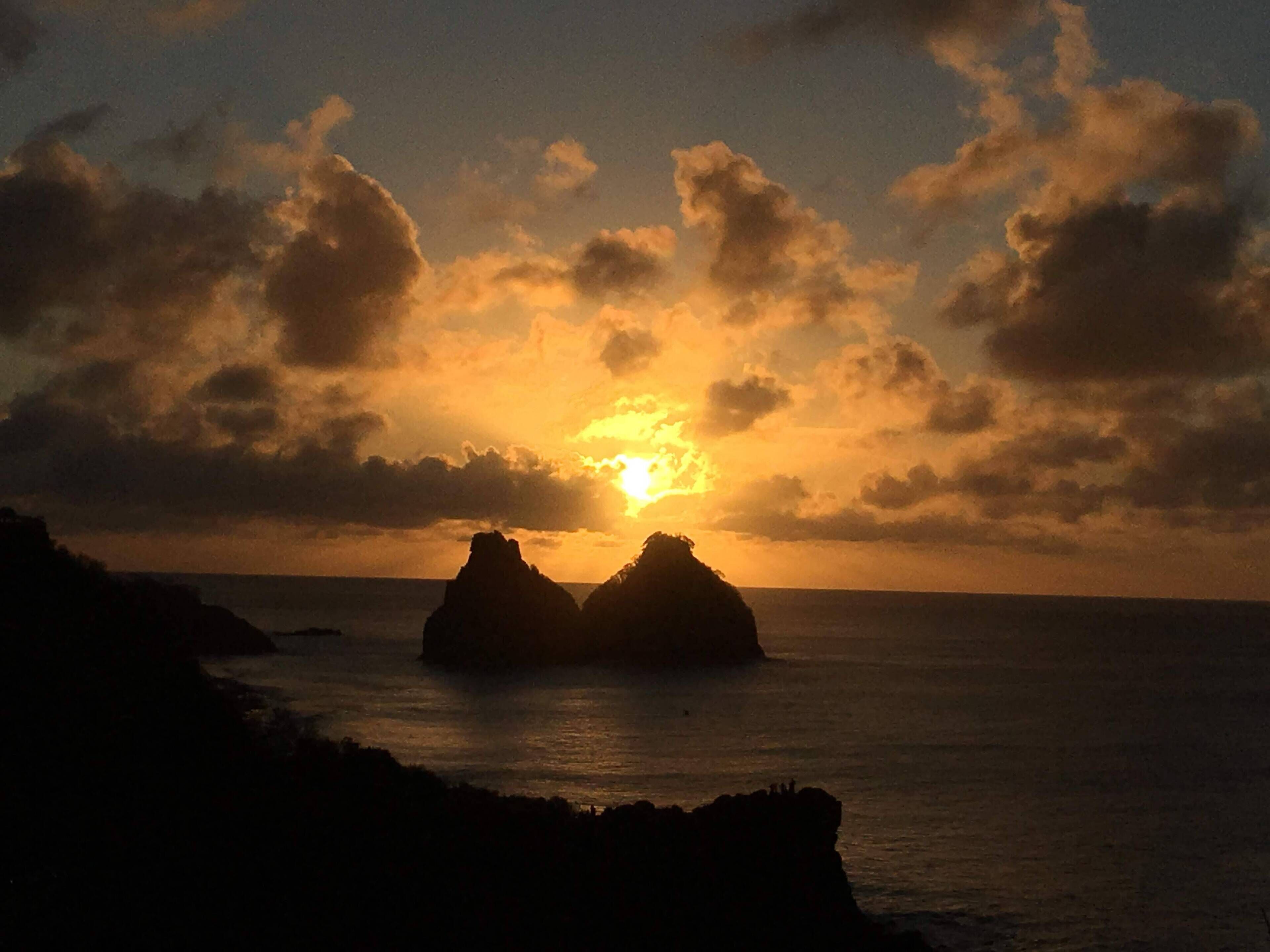 Tramonto su un paesaggio costiero con formazioni rocciose in silhouette contro il cielo.
