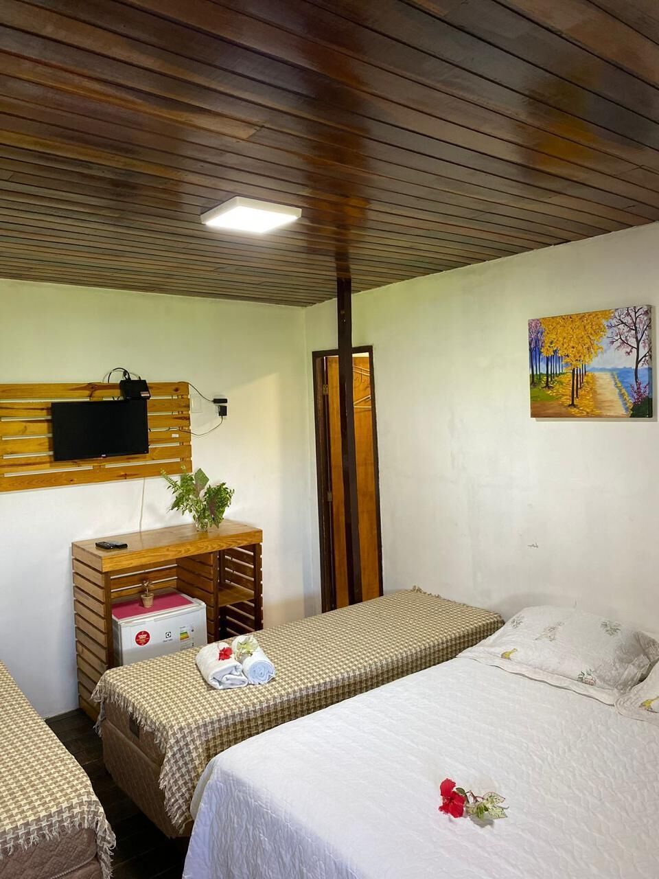 Una habitación con dos camas, un escritorio con televisor, un cuadro en la pared y un techo con vigas de madera.