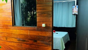 A wooden cabin with a window, a table with a white tablecloth, and a hanging light fixture. - Pousada Boldro Home (Fernando de Noronha)