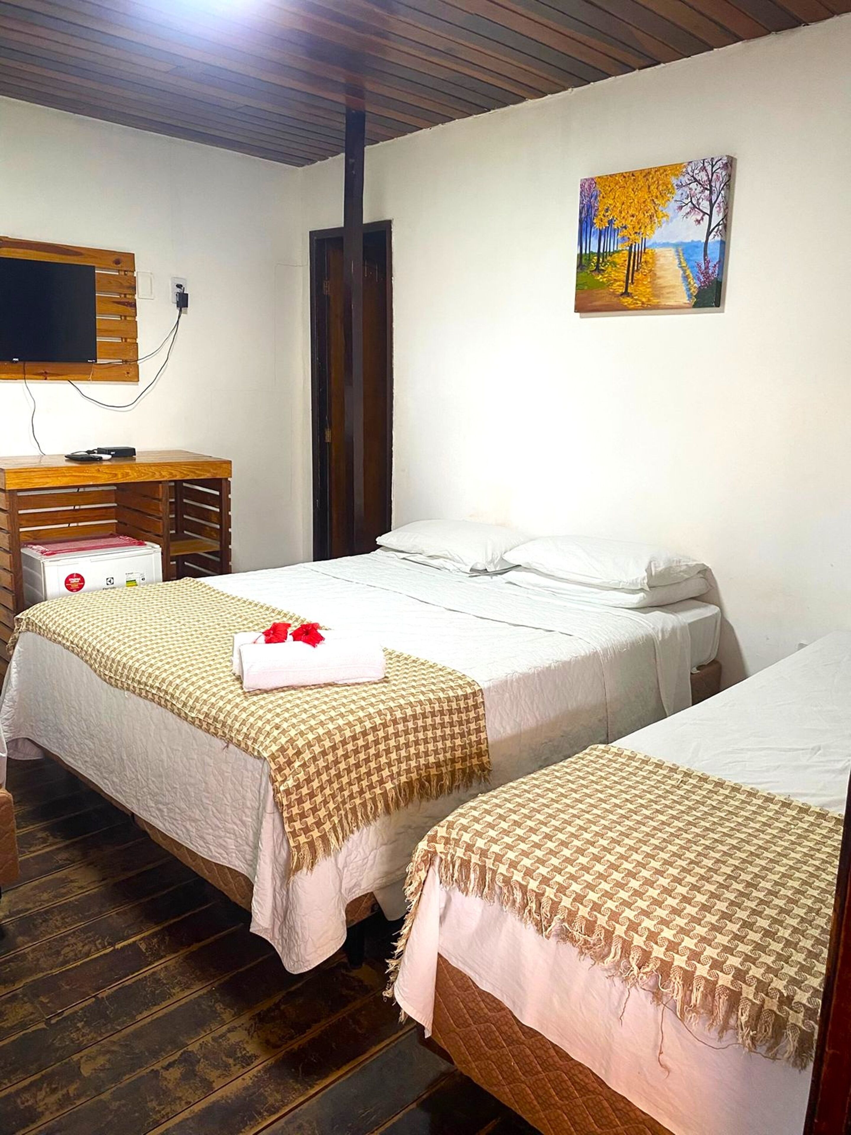 A room with two beds, a wooden desk, a television, and a painting on the wall.