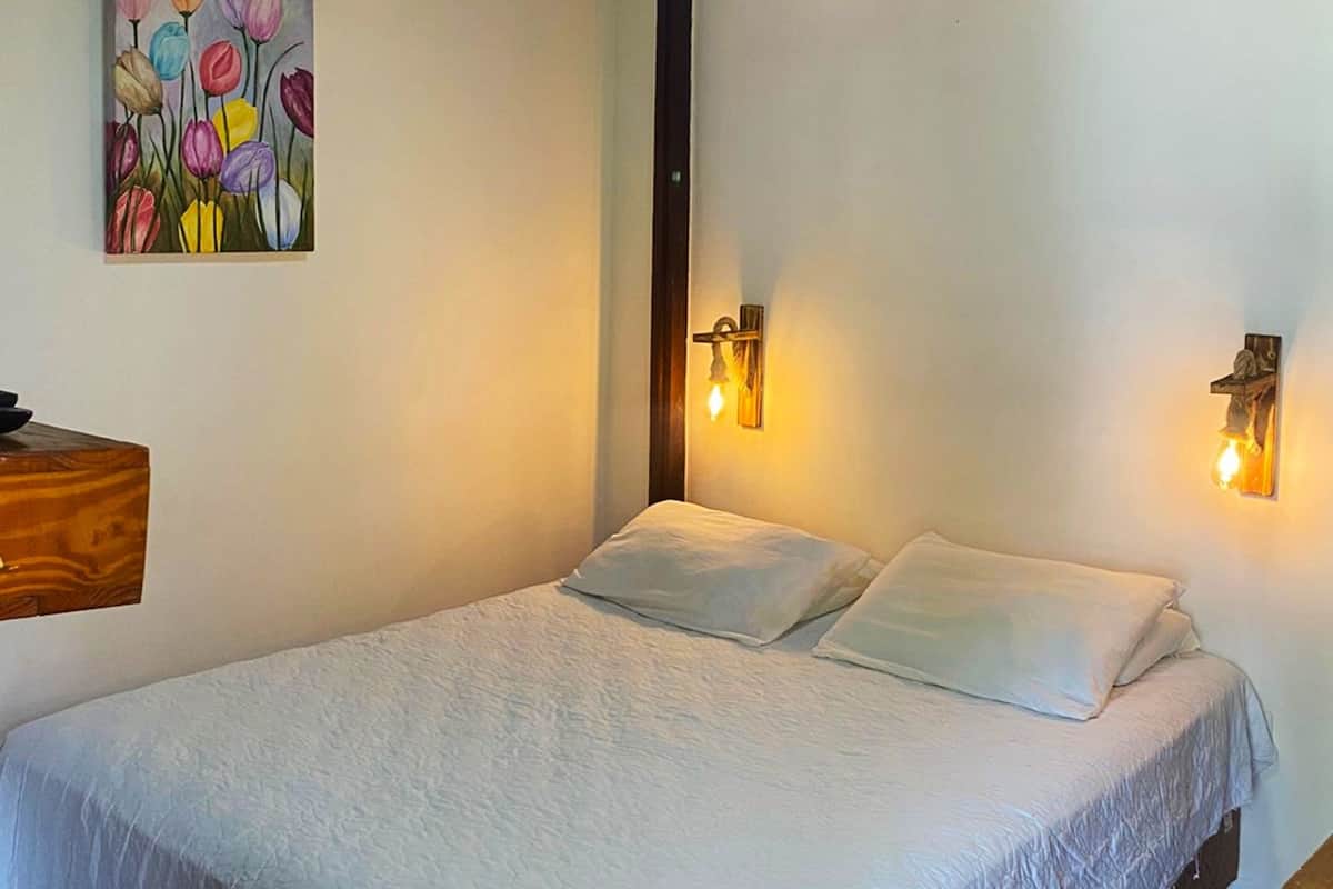 A bedroom with a bed, a painting, and two wall-mounted light fixtures.