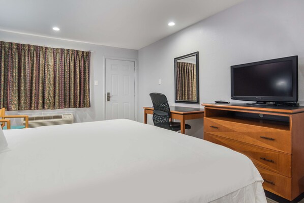 Habitación de hotel con una cama grande, un escritorio con silla, televisor y un espejo en la pared.