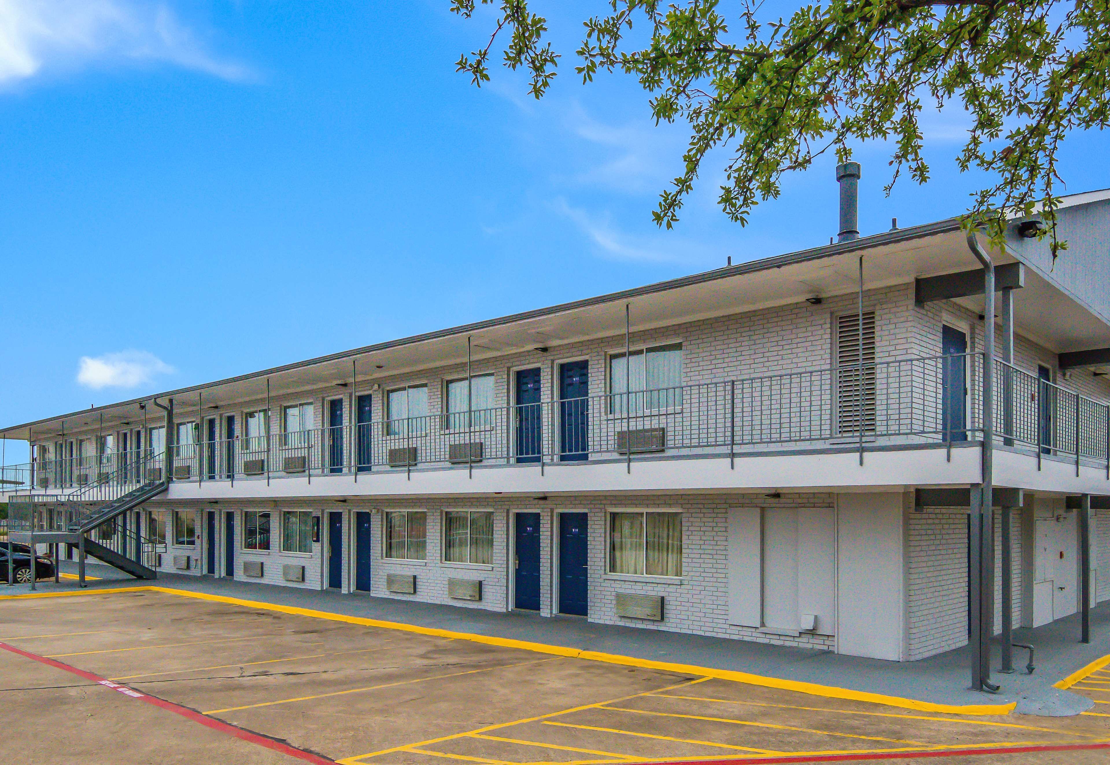 A two-story motel with a parking lot, a staircase to the upper level, and a brick facade.