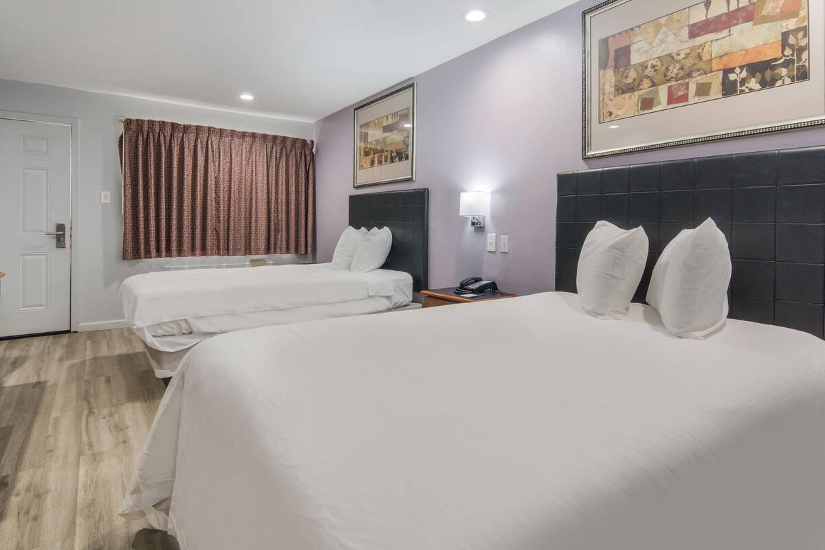 Habitación de hotel con dos camas, cabeceros, mesitas de noche, un cuadro enmarco y una puerta.