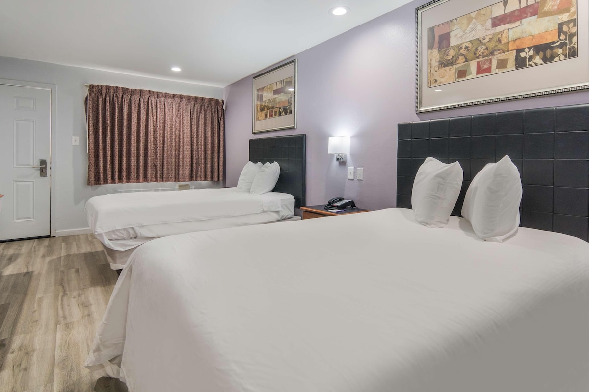 A hotel room with two beds, a large painting, a headboard, a nightstand, and a door.