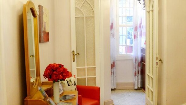 Una habitación con un tocador de madera, un espejo, un jarrón de flores rojas y una silla roja.