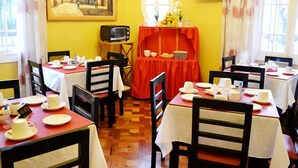 Un comedor con mesas dispuestas para dos, un cuadro en la pared, un televisor y una ventana con cortinas.