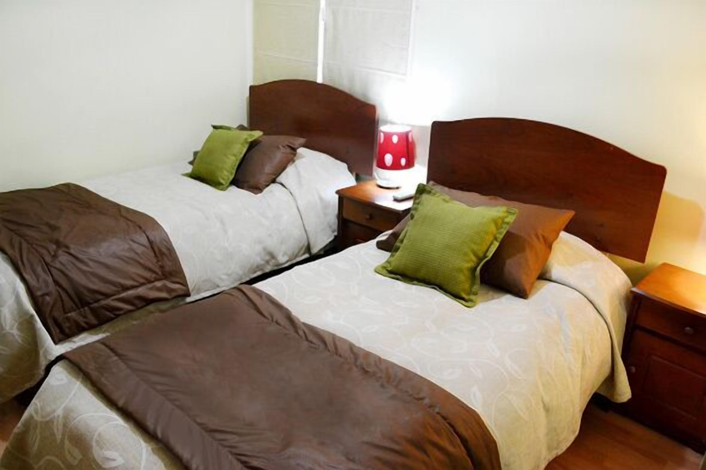 Una cama doble con ropa de cama marrón y beige, una mesita de noche con lámpara y una ventana con cortinas.