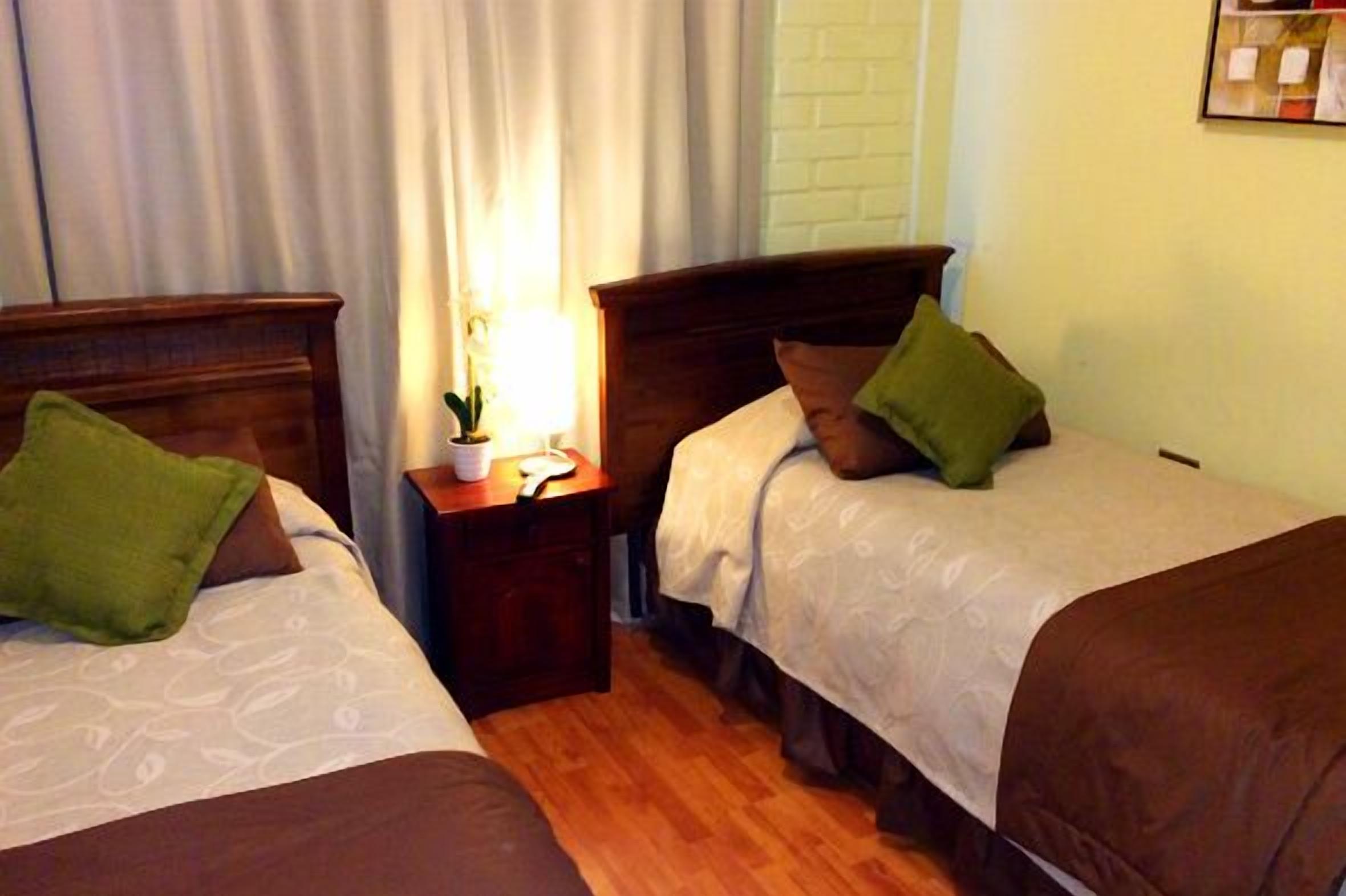 Een hotelkamer met twee eenpersoonsbedden, een nachtkastje met een lamp en een raam met gordijnen.