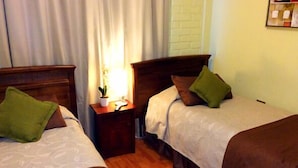 Una habitación de hotel con dos camas individuales, una mesita de noche con lámpara y una ventana con cortinas.