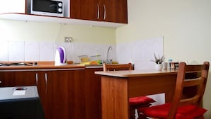 Cocina compacta con armarios de madera, microondas, fregadero y una zona de comedor con una silla.