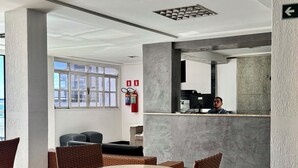 A modern interior with a round table and wicker chairs, a reception desk, and a fire extinguisher on the wall. - Las Brisas Beach Hotel (Natal)