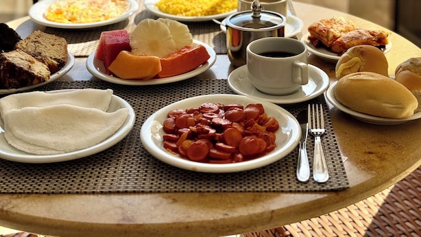 A breakfast table with various dishes, a coffee cup, and a view of a swimming pool. - Las Brisas Beach Hotel (Natal)