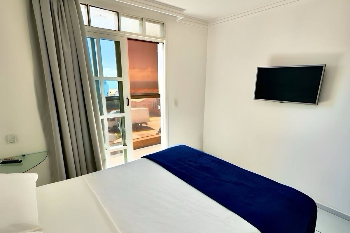 Une chambre d’hôtel avec un lit, un téléviseur fixé au mur et une fenêtre avec des rideaux.