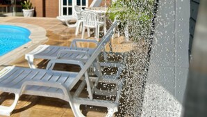 A poolside area with lounge chairs, a covered patio, and a house in the background. - Las Brisas Beach Hotel (Natal)
