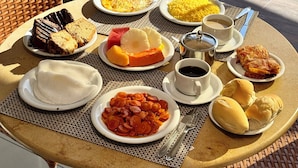 A table with various dishes and drinks, a wicker chair, and a view of a pool. - Las Brisas Beach Hotel (Natal)