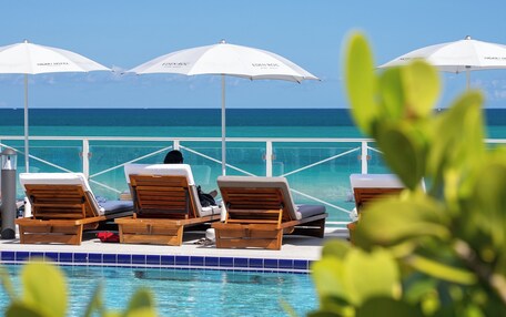 A poolside area with lounge chairs and umbrellas, overlooking a clear blue sea.