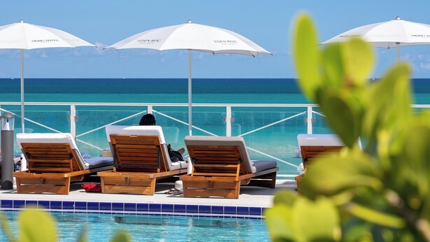 A poolside area with lounge chairs and umbrellas, overlooking a clear blue sea. - Nobu Hotel Miami Beach (Miami Beach)