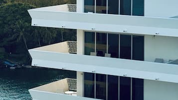 Un edificio moderno de varios pisos con balcones que dan a una masa de agua y un horizonte urbano al fondo.