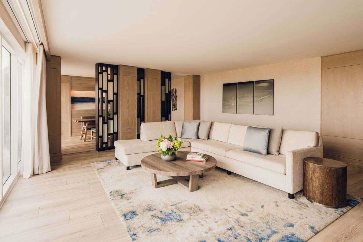 Una sala de estar moderna con un sofá color beige, una mesa de centro de madera y una alfombra estampada.