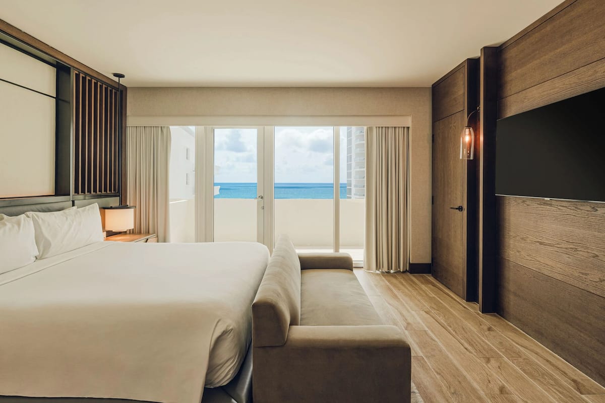 Habitación de hotel con una cama grande, un sofá, un televisor y vista al océano.