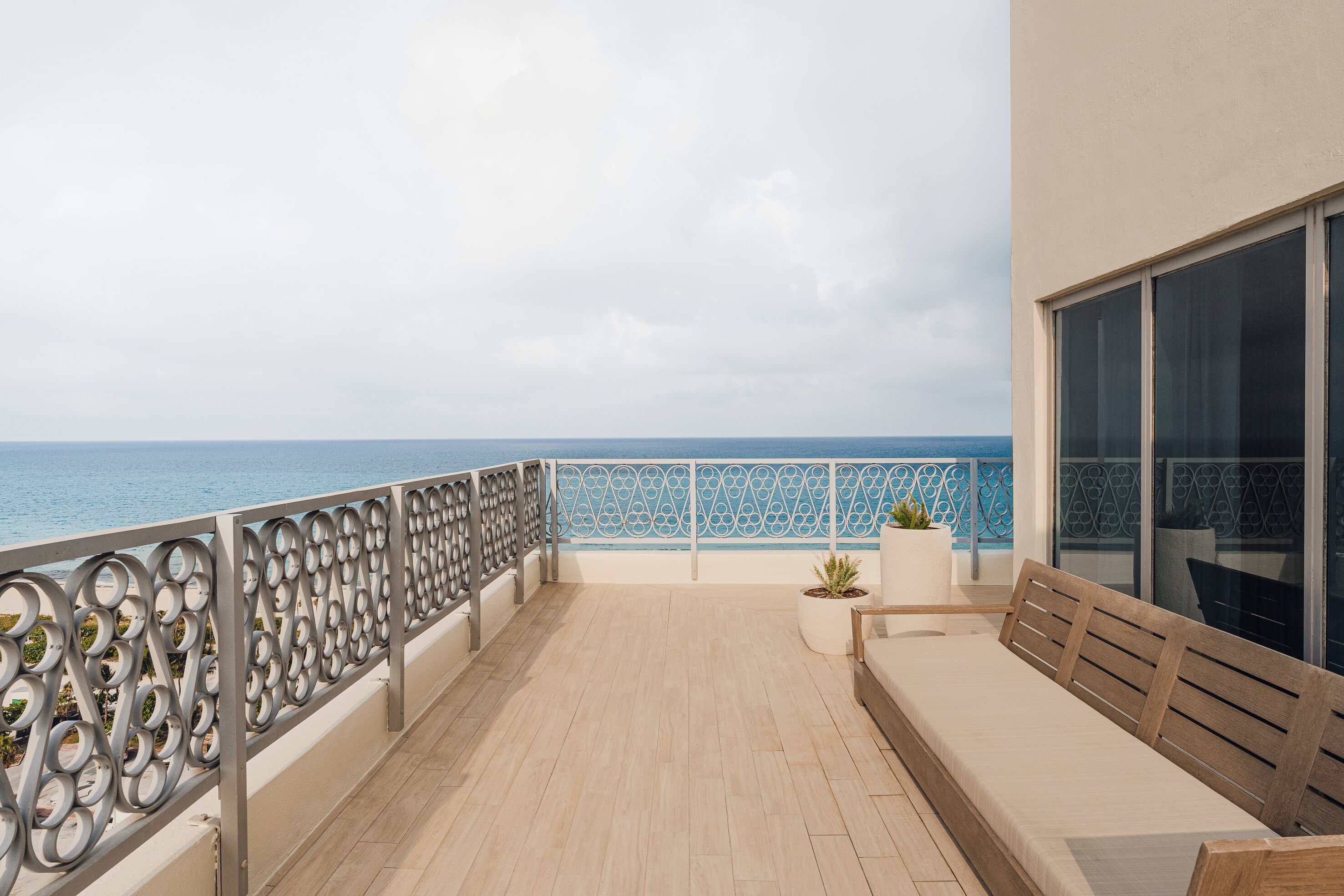 A balcony with a view of the sea, a wooden bench, and a potted plant.