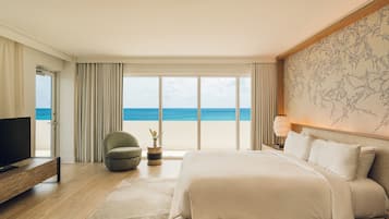 Una habitación de hotel moderna con una cama grande, televisión, un área de descanso con una silla y vista al océano.