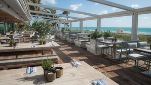 An outdoor dining area with wooden tables and white chairs, overlooking the ocean. - Nobu Hotel Miami Beach (Miami Beach)