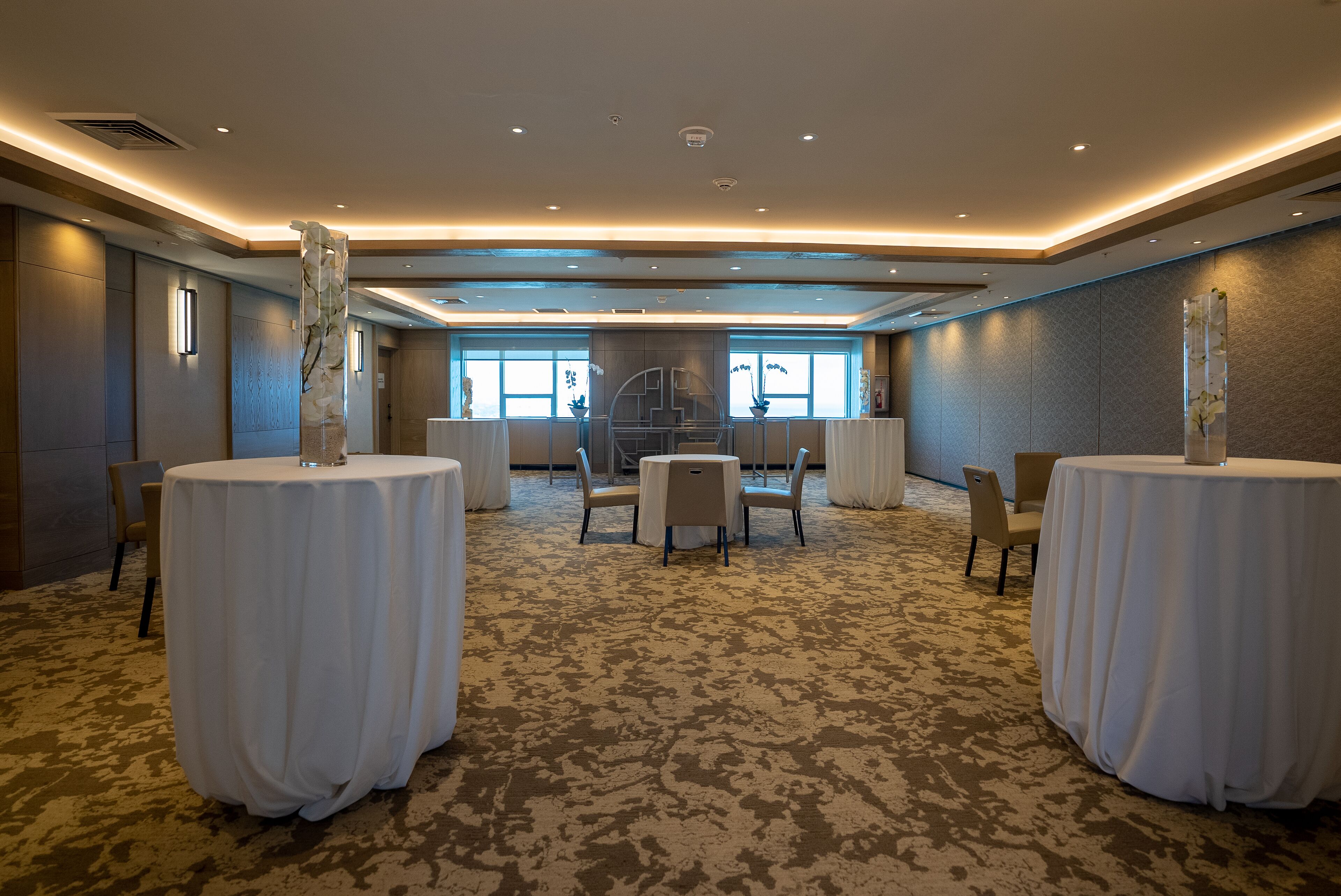 Una espaciosa sala de conferencias con mesas redondas, sillas y piso alfombrado.
