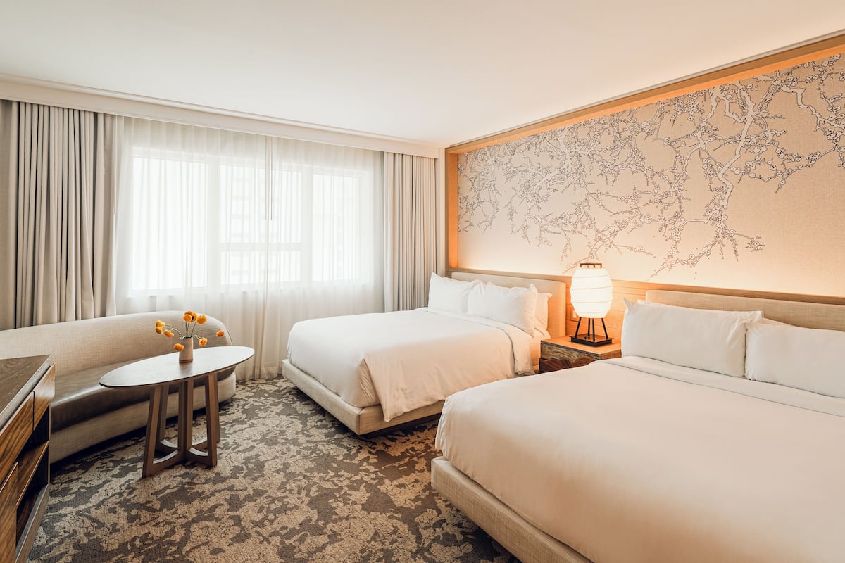 Habitación de hotel con dos camas, un sofá, una mesita con un florero y una obra de arte grande en la pared.