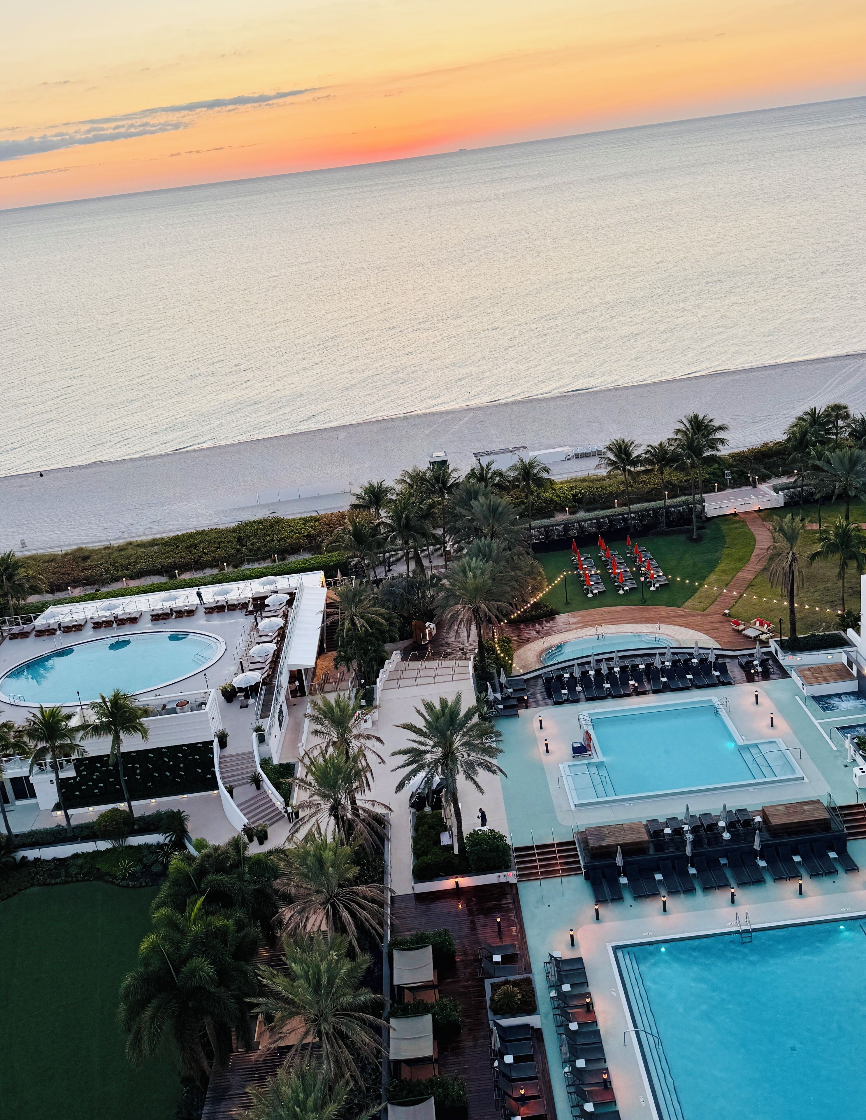 An aerial view of a resort with multiple swimming pools, palm trees, and a beach.