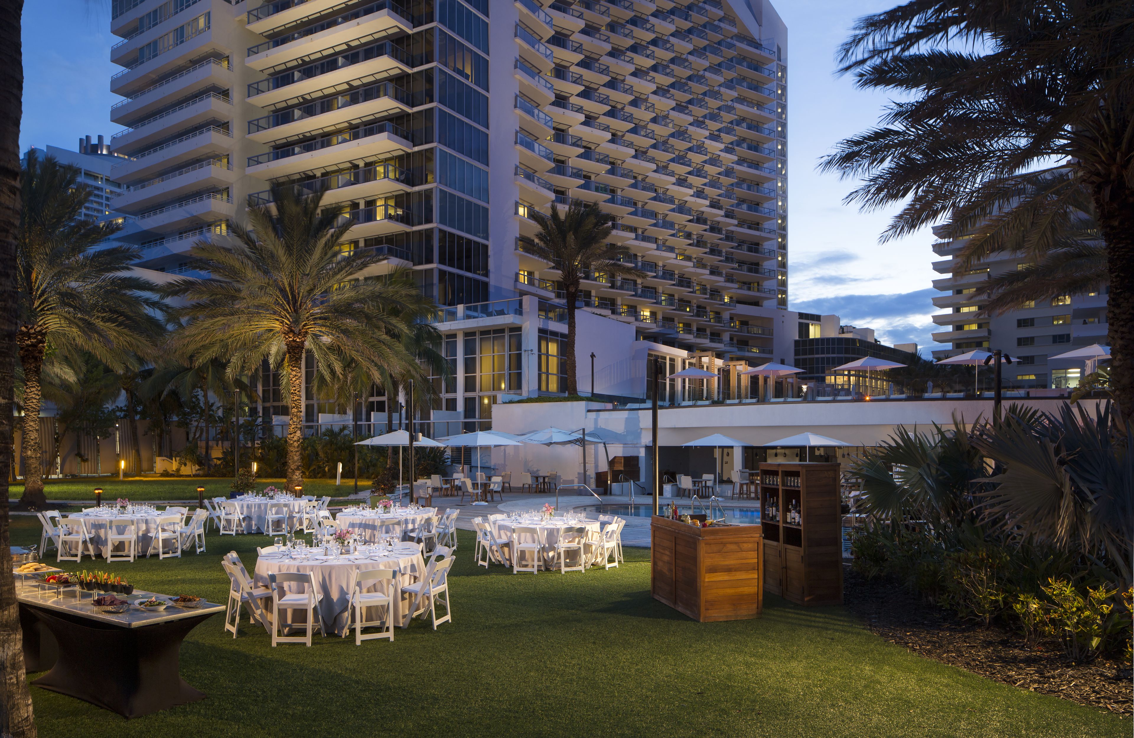 A hotel with outdoor dining areas, palm trees, and a pool.