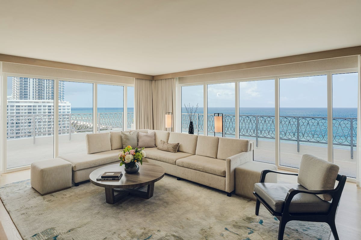 Un salón amplio con un ventanal que ofrece vistas al mar y un edificio de gran altura.