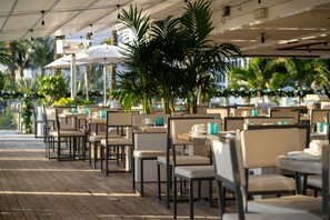 An outdoor dining area with tables and chairs, palm trees, and umbrellas. - Nobu Hotel Miami Beach (Miami Beach)