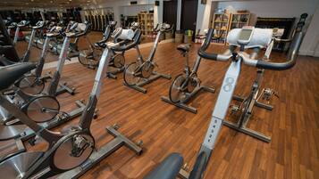 Un gimnasio con varias bicicletas estáticas, suelo de madera y equipamiento de ejercicio.