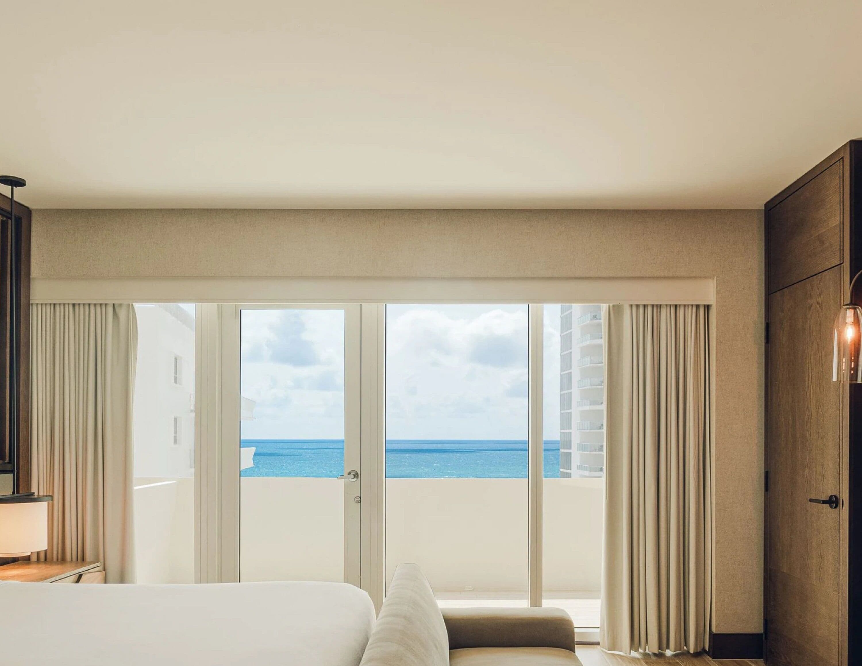 Habitación de hotel con un amplio ventanal corredero que da a un balcón con vista al océano.