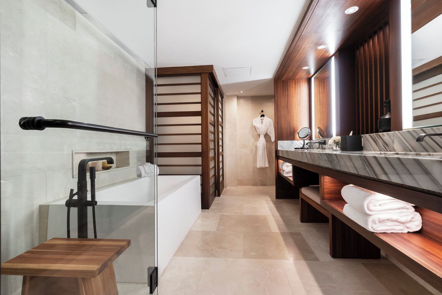 Une salle de bain moderne avec une douche à parois de verre, un banc en bois, un lavabo en marbre et un porte-peignoir.