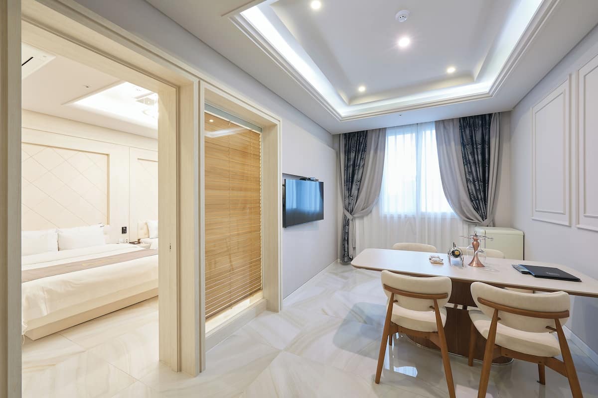 Quarto de hotel moderno com cama, televisão, área de refeições com cadeiras e mesa.