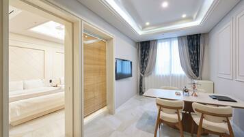 A modern hotel room with a bed, a TV, a dining area with chairs, and a table.