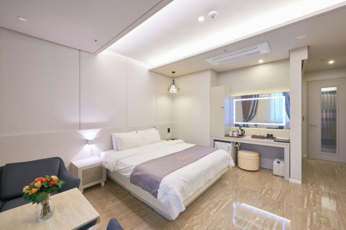 Une chambre d’hôtel moderne équipée d’un lit, d’une table de chevet, d’une lampe et d’un petit bureau avec un miroir.