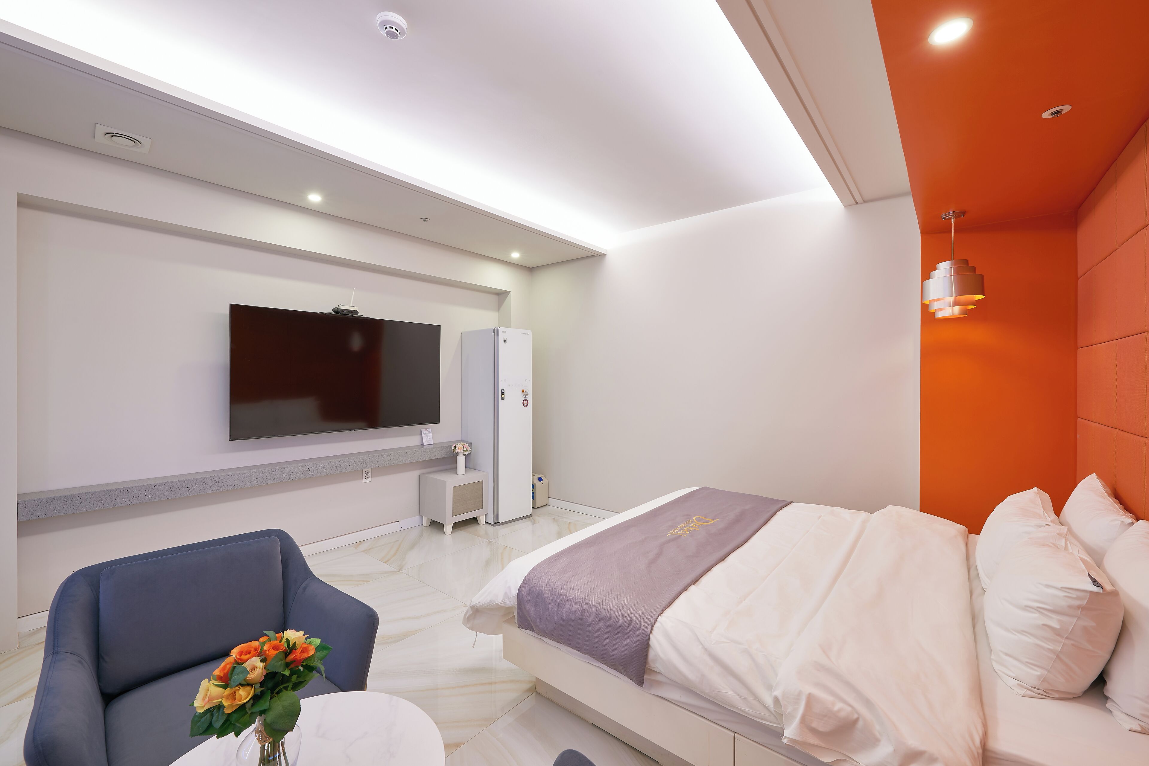 A modern hotel room with a bed, a TV, a desk, and a chair.
