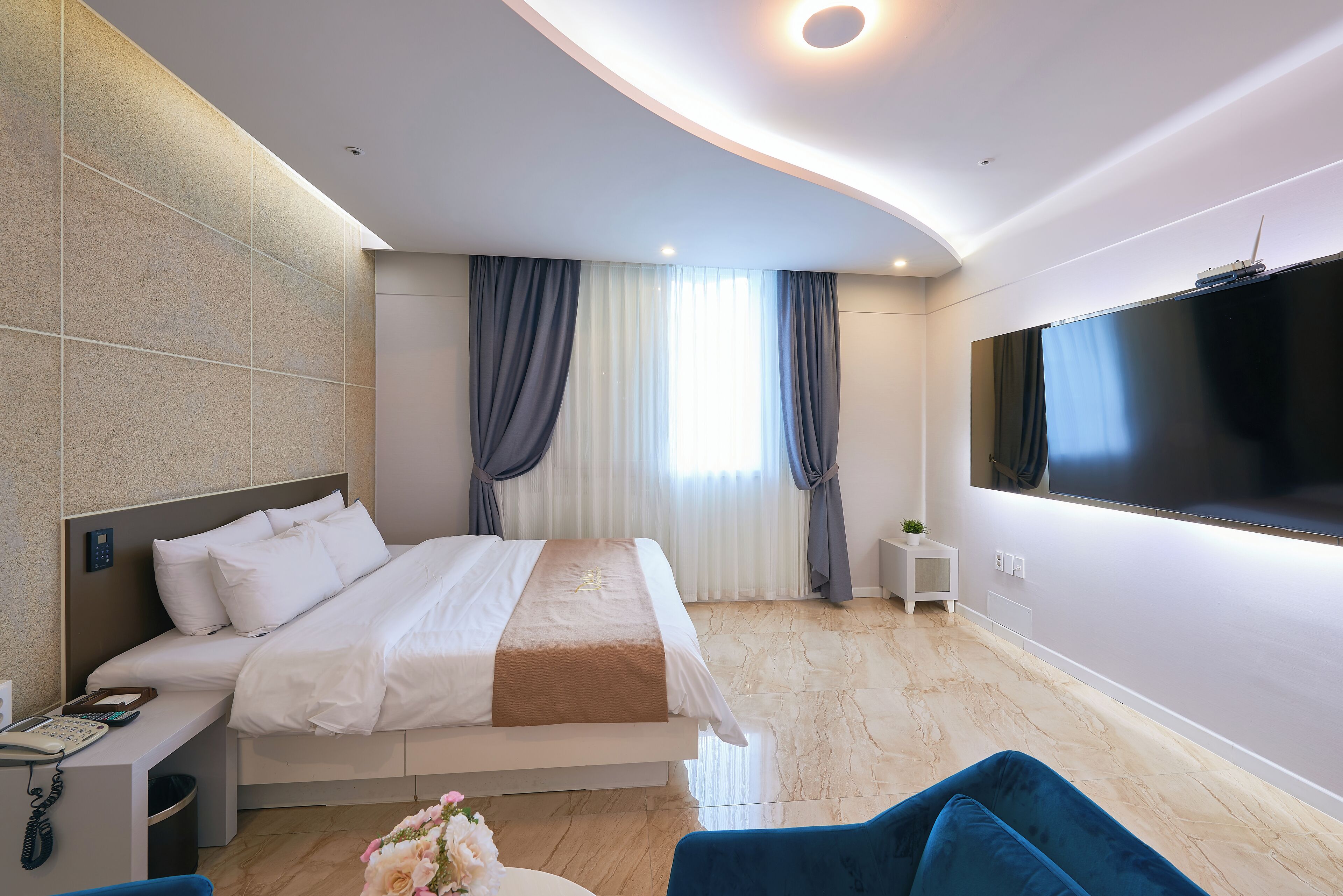 Een moderne hotelkamer met een groot bed, een bureau met telefoon, een aan de muur bevestigde televisie en een klein bijzettafeltje.