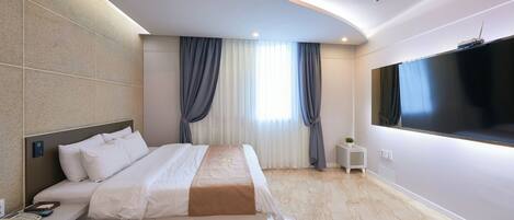 A modern hotel room with a large bed, a desk with a phone, a TV mounted on the wall, and a small side table.