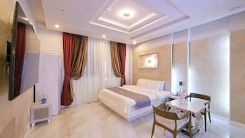 A modern hotel room with a large bed, bedside table, and a small dining area with a table and chairs.