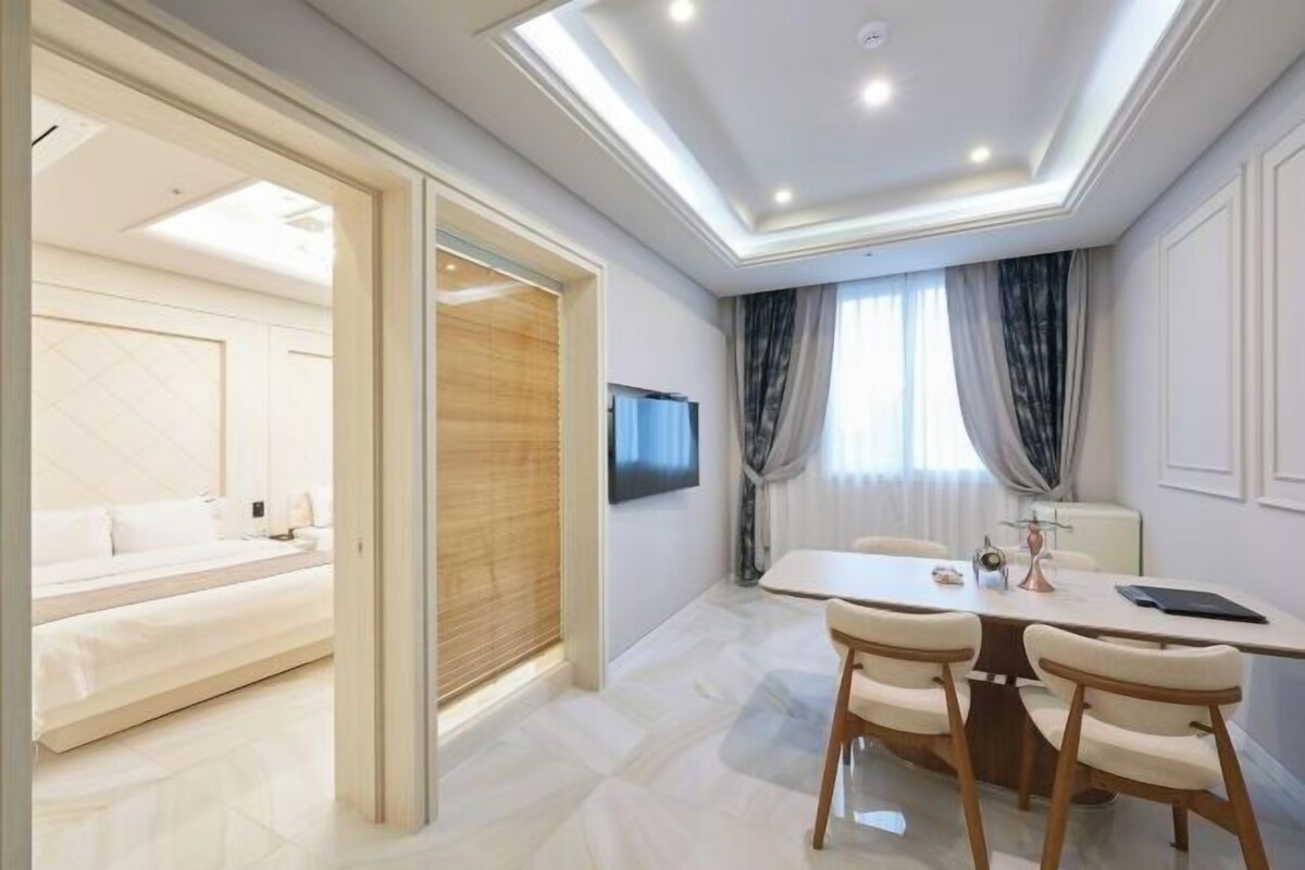 Une chambre d’hôtel moderne comprenant un lit, un coin repas avec une table et des chaises, et un téléviseur fixé au mur.