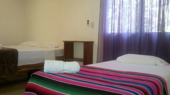 Een hotelkamer met twee bedden, een klein nachtkastje en een raam met gordijnen.