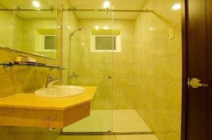 A bathroom with a glass-enclosed shower, a sink with a marble countertop, and a small window above the shower.