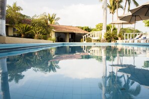Una piscina con bordes de azulejos, rodeada de palmeras y un edificio con tejado de tejas.